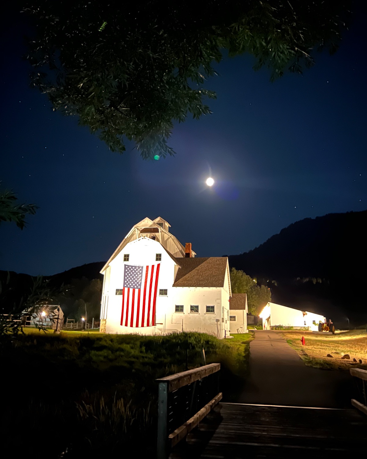 A white barn with an American flag under a full moon, and the bridge to it